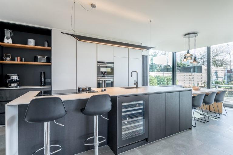 Strakke keuken met groot kookeiland, wijnkoeler en glaswand